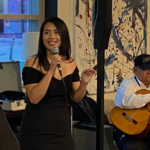Marlén Mendoza speaks to an audience in front of local musicians for the public launching of Emprendimiento Latino 5M, a new organization dedicated to Latino entrepreneurs.
