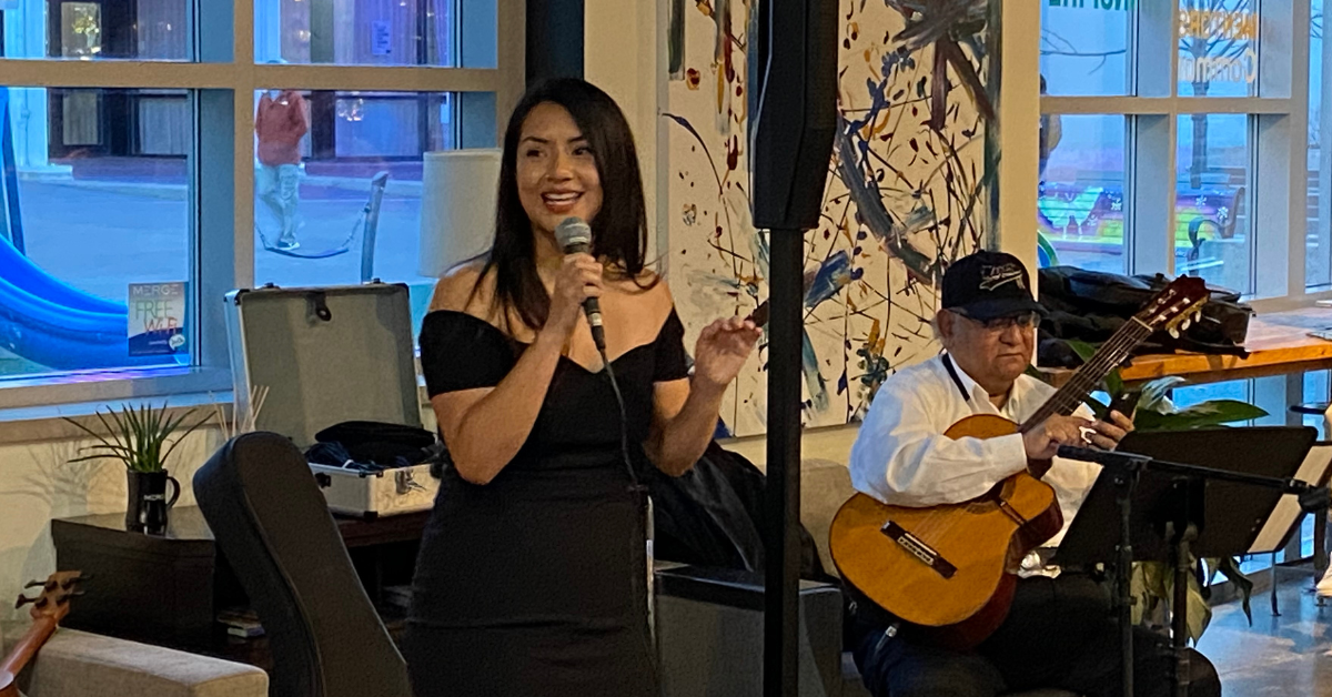 Marlén Mendoza speaks to an audience in front of local musicians for the public launching of Emprendimiento Latino 5M, a new organization dedicated to Latino entrepreneurs.