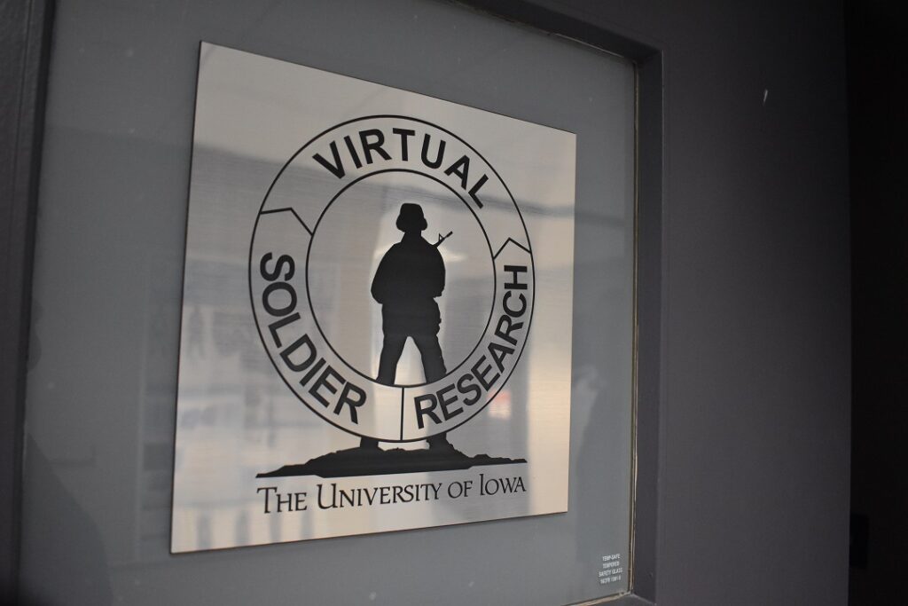 A metallic sign on a door has a silhouette of a soldier holding a gun. A circle goes around the soldier with the words "Virtual Soldier Research."