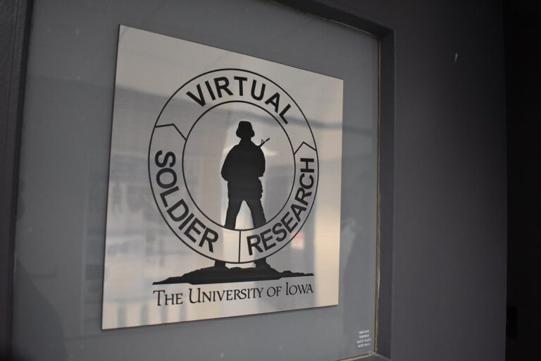 A metallic sign on a door has a silhouette of a soldier holding a gun. A circle goes around the soldier with the words "Virtual Soldier Research."