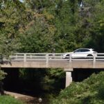 A car drives past a pedestrian on the Gilbert Street bridge.