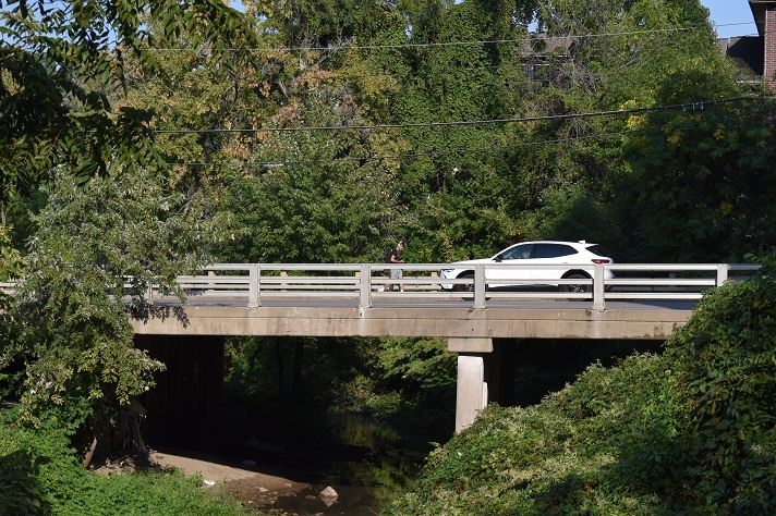 A car drives past a pedestrian on the Gilbert Street bridge.