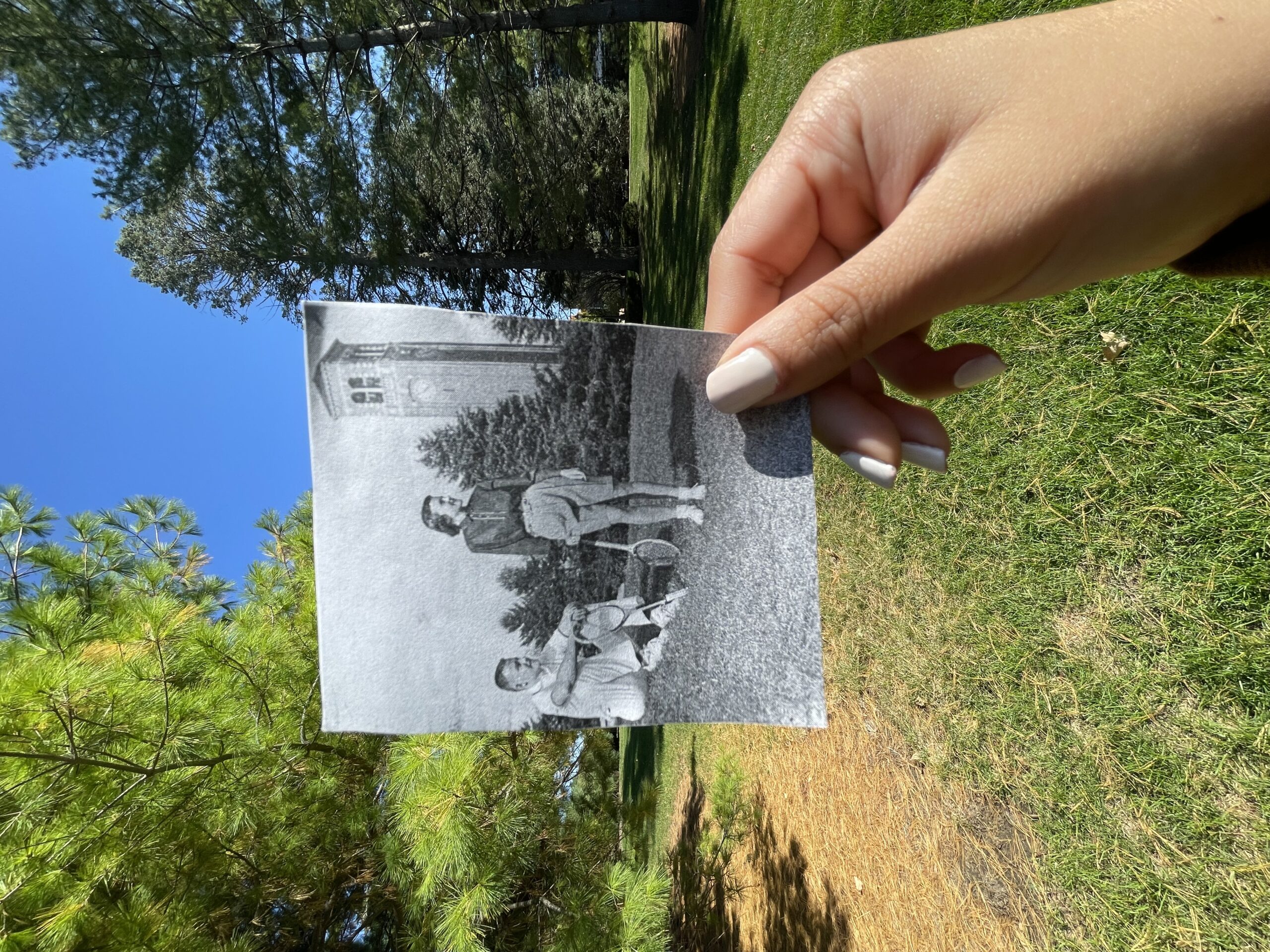 A hand holds a black and white photograph against the current location where the photo was taken.