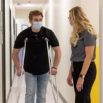 A patient in crutches is helped by a staff member at uihc