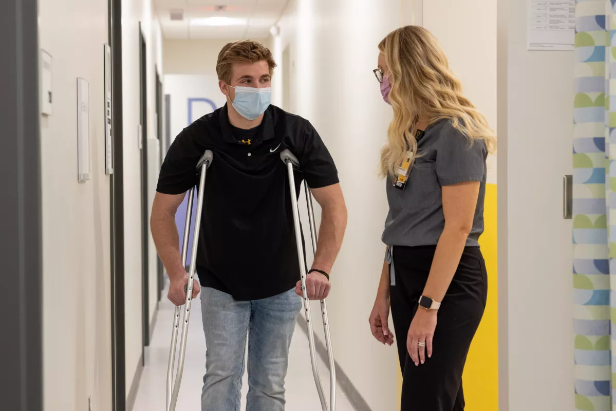 A patient in crutches is helped by a staff member at uihc