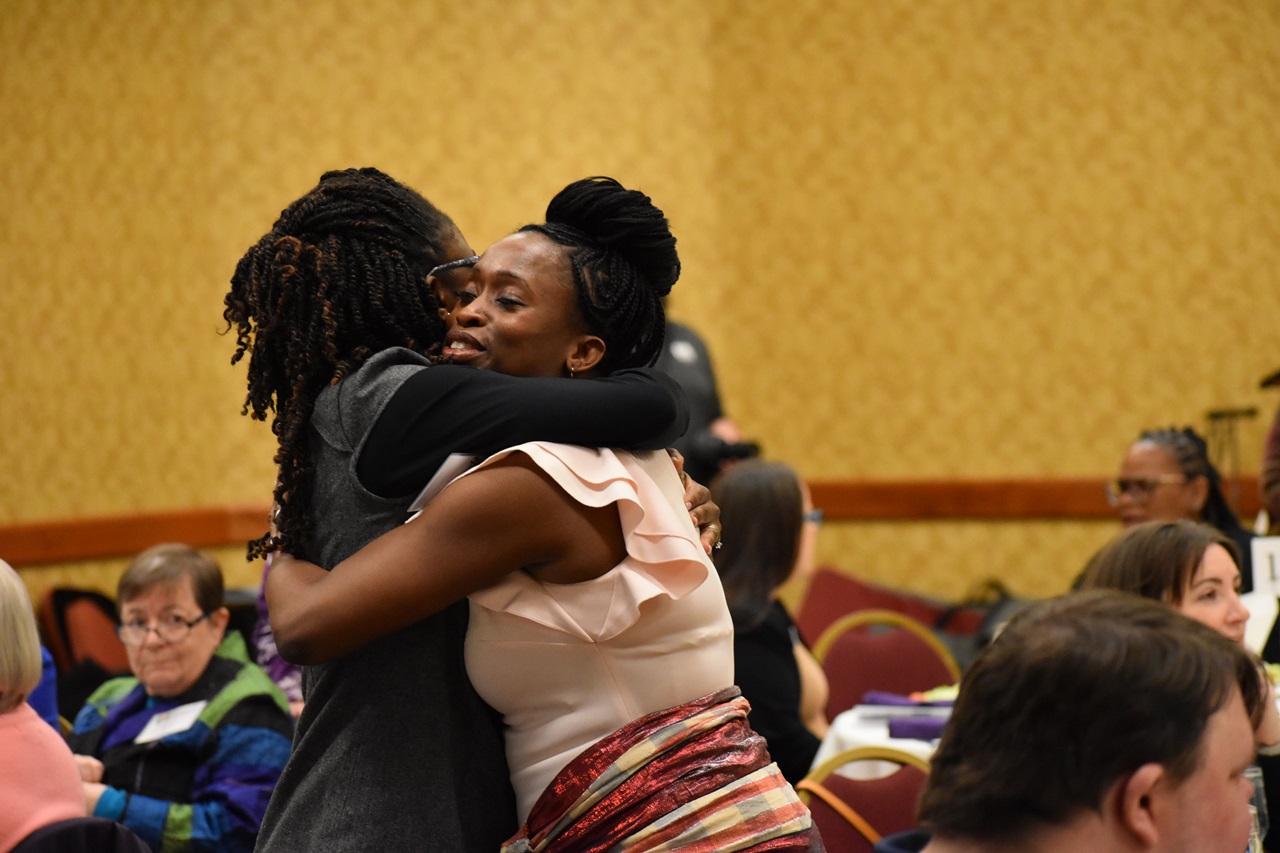 Two women embrace at the Catherine McAuley Center Immigration & Business Luncheon Awards, at the Radisson Hotel Cedar Rapids.