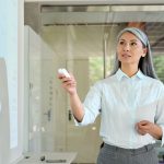 Confident mid age Asian businesswoman corporation leader presenting successful project financial results talking to audience pointing standing at board room in modern office. Business career concept.