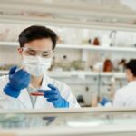 A scientist wearing a face mask and lab coat holds a petri dish.