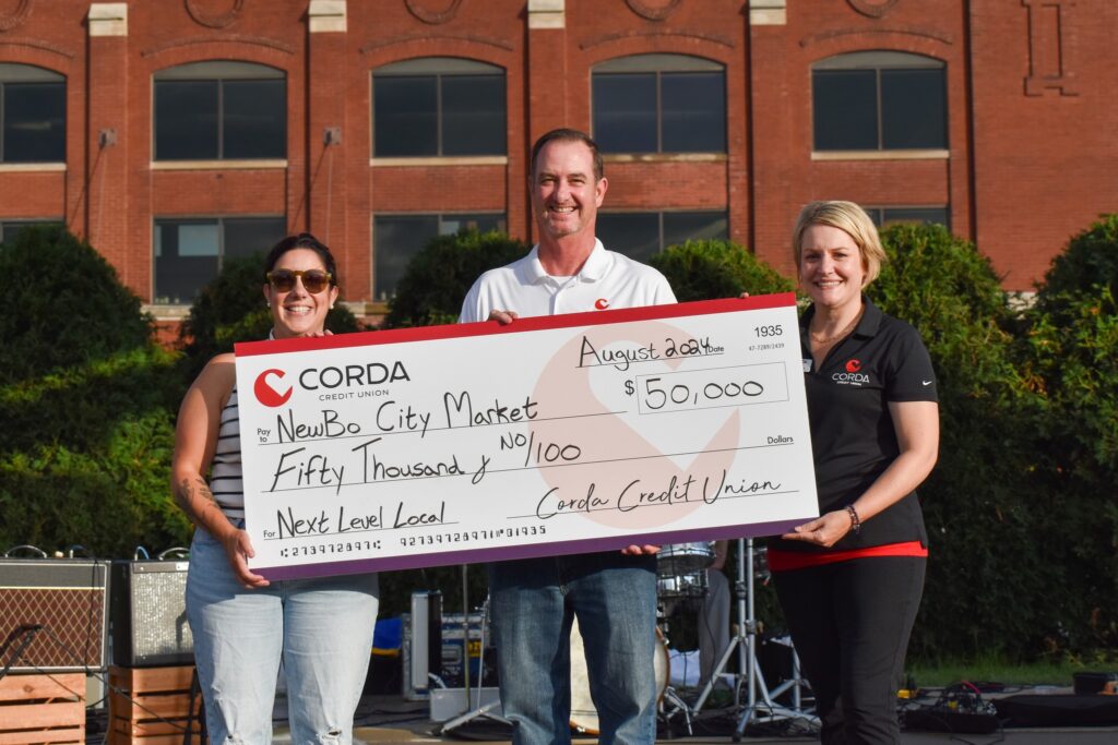 Corda Credit Union representatives present NewBo City Market Executive Director Julie Parisi with a check representing a $50,000 donation to the organization's Next Level Local capital campaign.