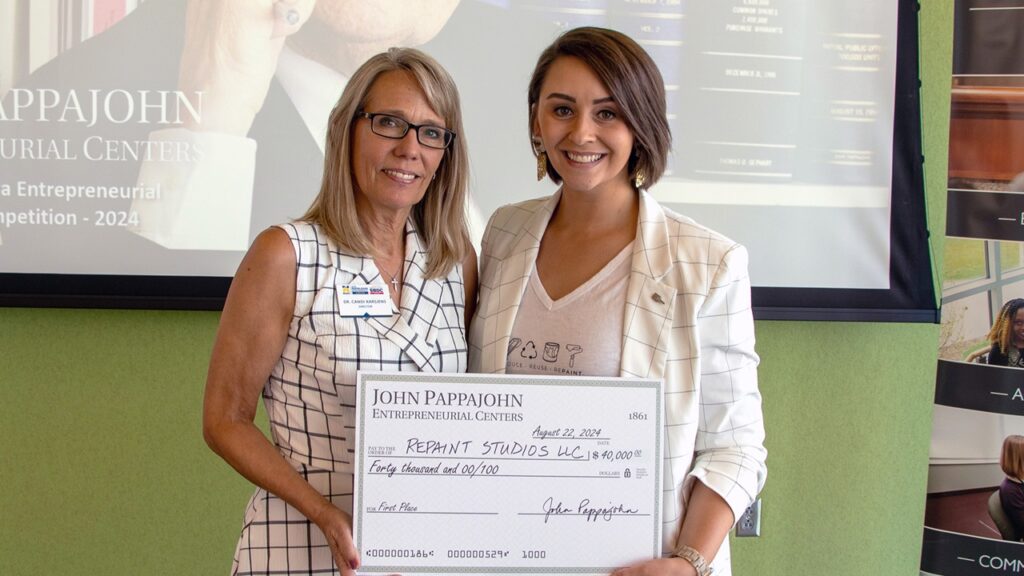 Candi Karsjens, director for the North Iowa Area Community College JPEC, presents Repaint Studios owner Billie Kay Ingalls Asmus with a check.