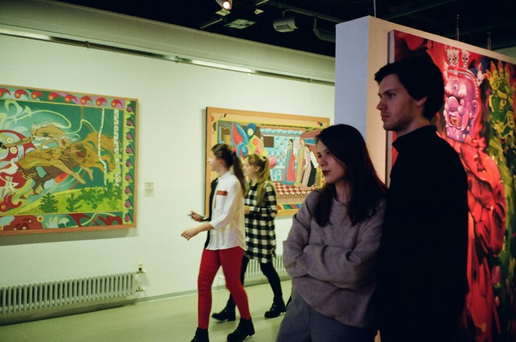 A young man and woman examine paintings in an art gallery.