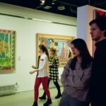 A young man and woman examine paintings in an art gallery.
