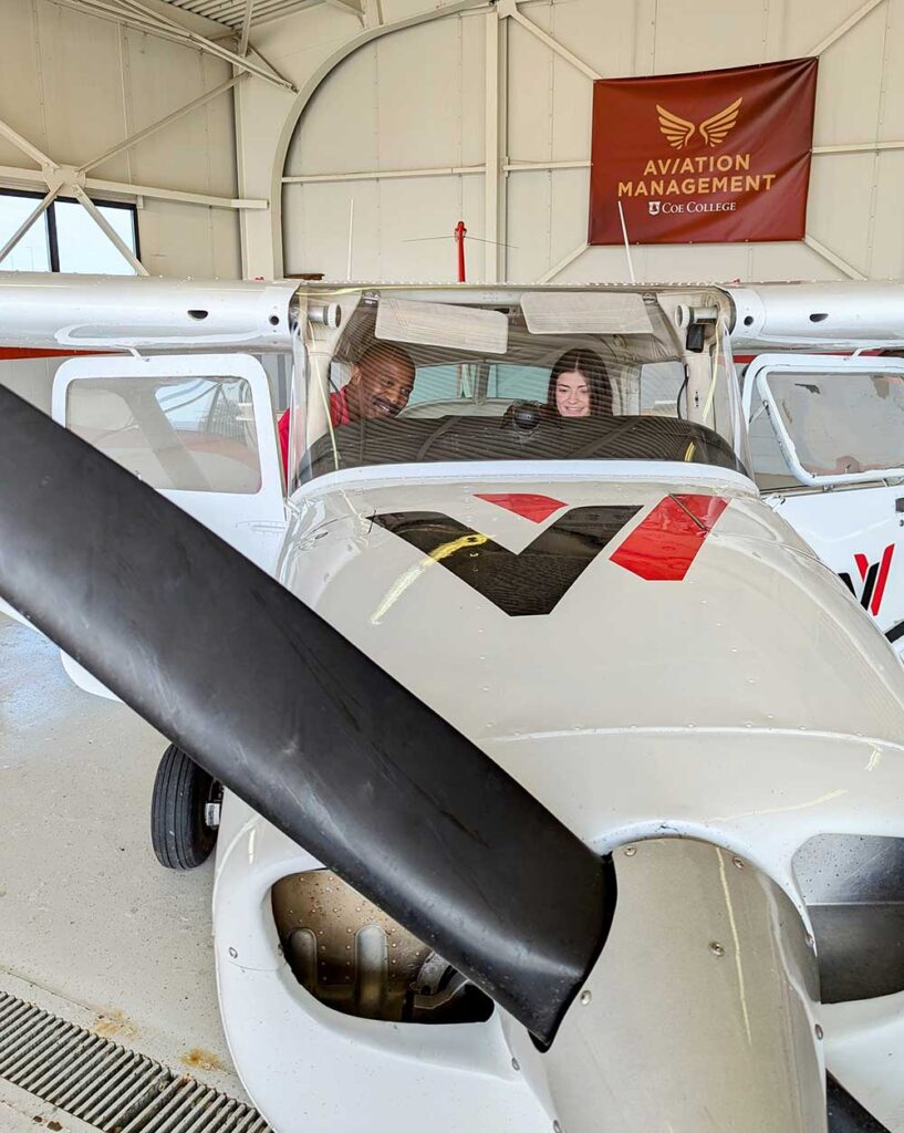 A Coe College student sits in a Revv airplane within a hangar.