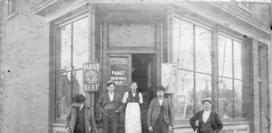 A historical photo shows George Buffon – wearing a white apron – standing in front of the saloon he owned at 401 E Market St, Iowa City, in 1899. The identities of the others in this photo are unknown. CREDIT JOHN’S GROCERY ARCHIVES