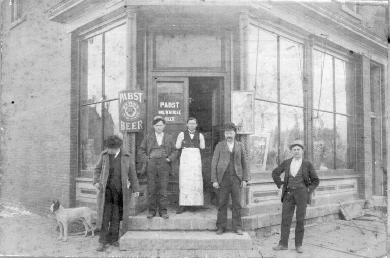 A historical photo shows George Buffon – wearing a white apron – standing in front of the saloon he owned at 401 E Market St, Iowa City, in 1899. The identities of the others in this photo are unknown. CREDIT JOHN’S GROCERY ARCHIVES