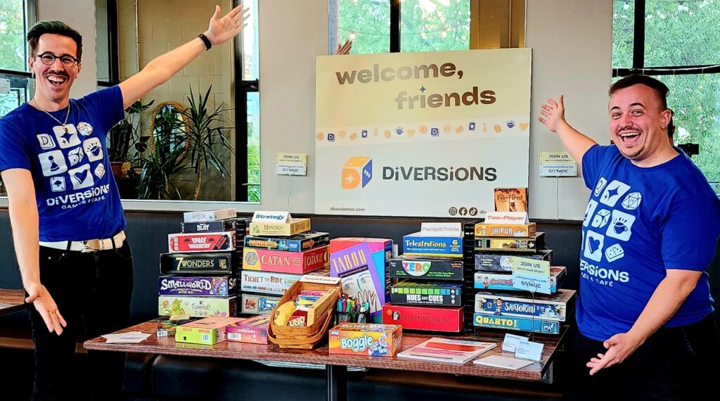 Diversions Tabletop game Lounge co-owners Sean Finn and Nolan Petersen pose next to a stack of board games.