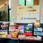 Diversions Tabletop game Lounge co-owners Sean Finn and Nolan Petersen pose next to a stack of board games.