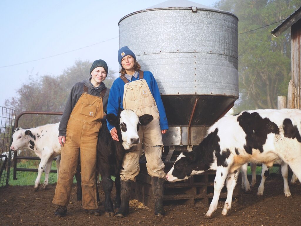 Shae and Anna Pesek of Over the Moon Farm pose with two calves on their farm.