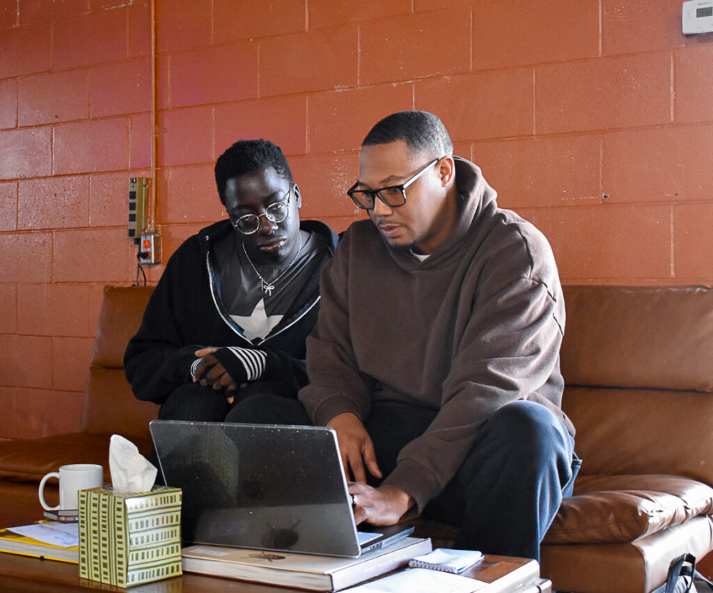 Graphic design apprentice Wisdom Konu (left) looks over André Wright’s shoulder as the two discuss Mr. Konu’s progress in the program. CREDIT ANNIE SMITH BARKALOW