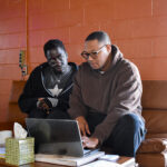 Graphic design apprentice Wisdom Konu (left) looks over André Wright’s shoulder as the two discuss Mr. Konu’s progress in the program. CREDIT ANNIE SMITH BARKALOW