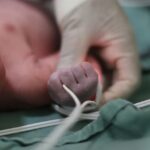 A medical professional grasps a newborn baby's wrist.