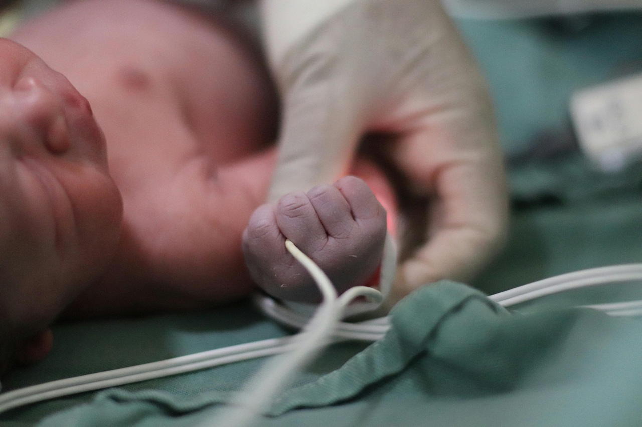 pexels-gabi-orrico-194178369-28206179 A medical professional grasps a newborn baby's wrist.
