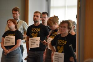 Members of COGS -- Campaign to Organize Student Workers -- gather at the back of a meeting room at the Levitt Center for University Advancement during the June 11 Board of Regents meeting. The protestors wore placards declaring "Hands off: Tuition & Fees, Academic Freedom, DEI."