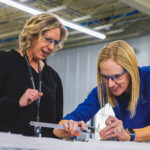 Crystal Group director of production Kara Kortenkamp and supply chain director Katie Wagner validate dimensions on a machined metal component at the company’s Hiawatha facility. CREDIT CRYSTAL GROUP manufacturing
