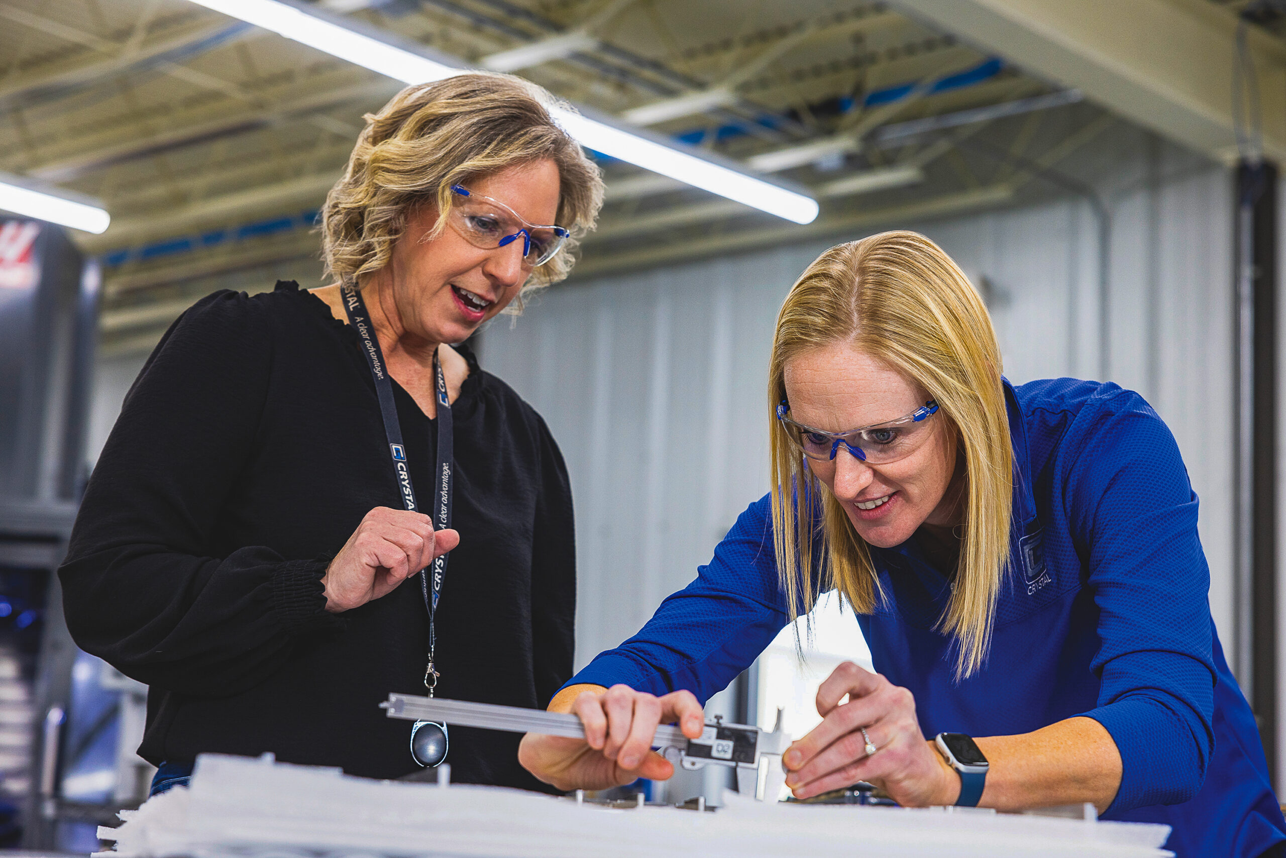 Monga-10 Crystal Group director of production Kara Kortenkamp and supply chain director Katie Wagner validate dimensions on a machined metal component at the company’s Hiawatha facility. CREDIT CRYSTAL GROUP manufacturing