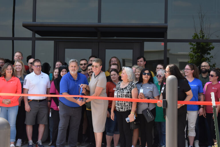 CIVCO Medical Solutions President Robin Therme (center) readies a giant pair of scissors for the ribbon-cutting ceremony celebrating the company's new facility on June 6.