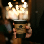 Midnight Coffee's logo is prominently displayed on a disposable coffee cup.