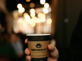 Midnight Coffee's logo is prominently displayed on a disposable coffee cup.