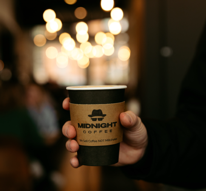 Midnight Coffee's logo is prominently displayed on a disposable coffee cup.
