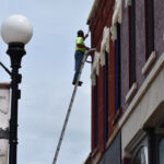A painter on an extension ladder works on a second story building facade in downtown Anamosa on July 8, 2025.