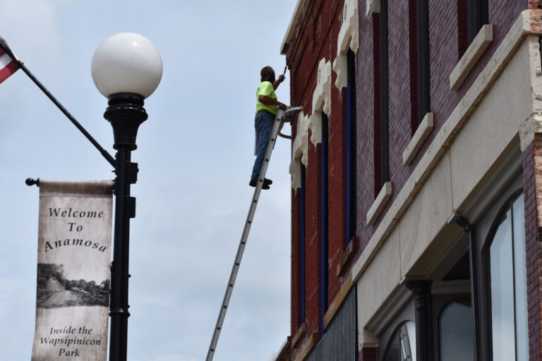 A painter on an extension ladder works on a second story building facade in downtown Anamosa on July 8, 2025.