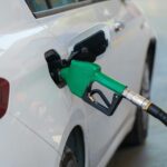 The green handle of a gas pump is inserted into a car's fuel tank.