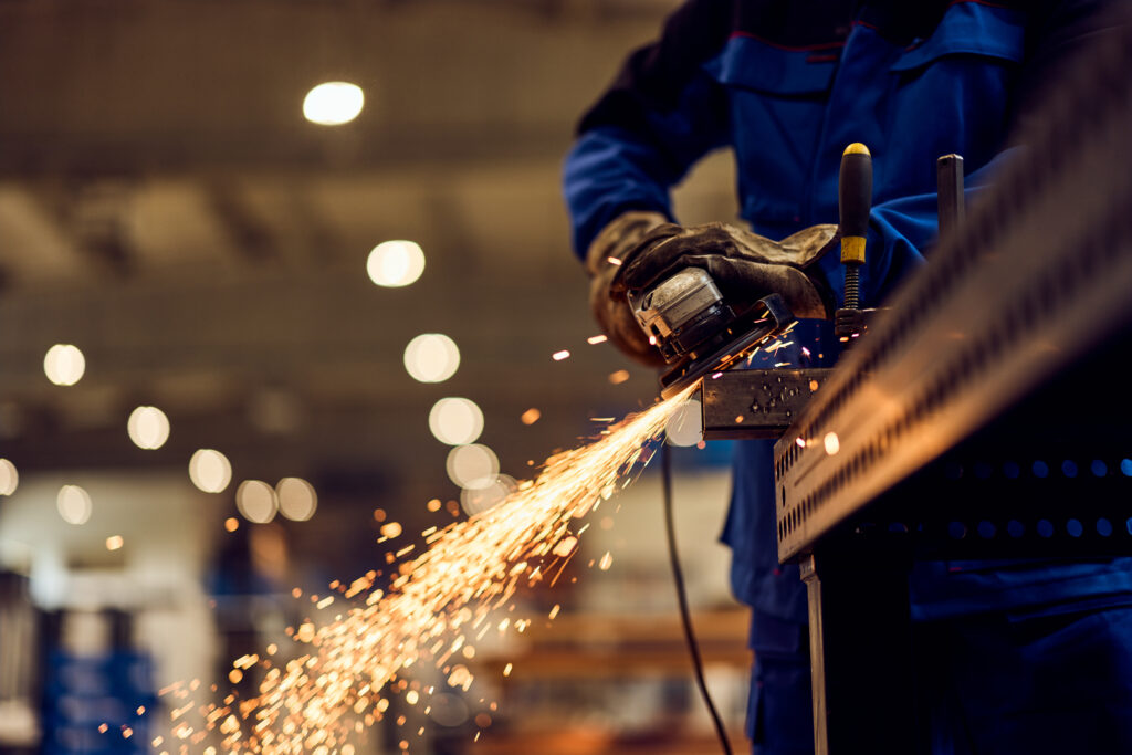 Worker performing grinding task in an industrial setting with bright flying sparks. CREDIT HOLMES MURPHY