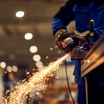 Worker performing grinding task in an industrial setting with bright flying sparks. CREDIT HOLMES MURPHY