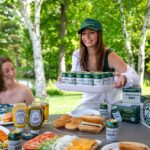 A smiling woman brings a tray of Neighborhood Beer to some women sitting at a picnic table.